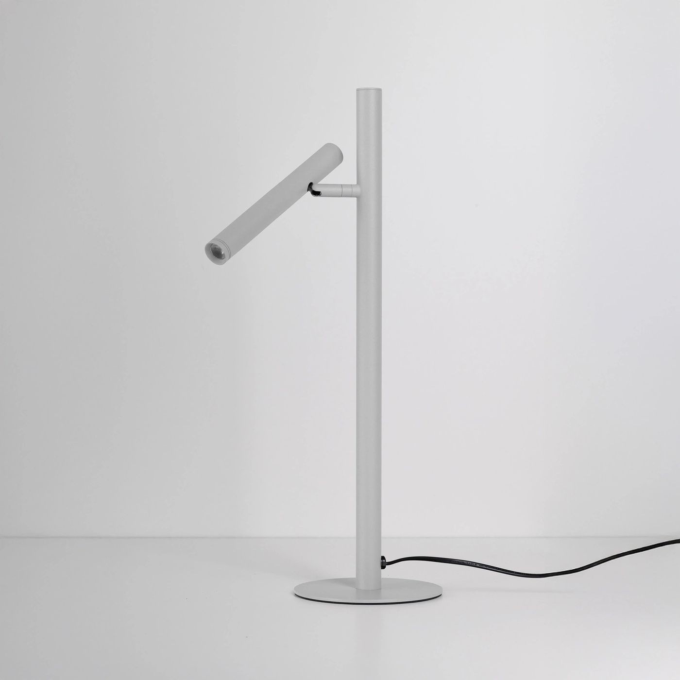 Lampa stołowa LED Trost, moc 4,5W, w kolorze białym. Posiada smukły, cylindryczny klosz montowany na stalowym, prostym stelażu z okrągłą podstawą. Ujęcie z boku, na jednolitym jasnym tle, widoczny kabel zasilający.