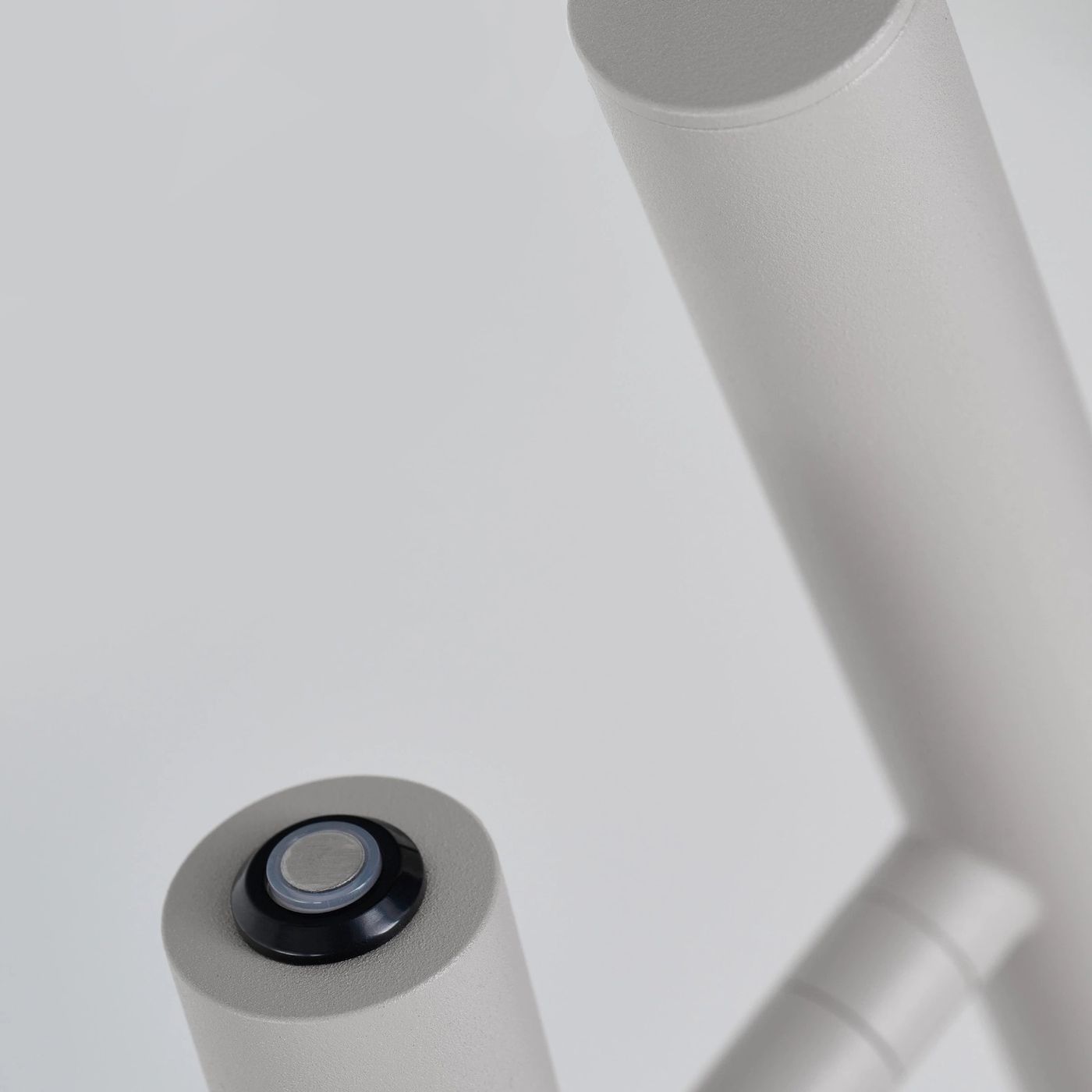Lampa stołowa LED Trost 4,5W w białej obudowie, widok z góry na przycisk włączający z metalowym wykończeniem. Produkt ma prostą, cylindryczną formę z matową fakturą. Tło jasne, jednolite.