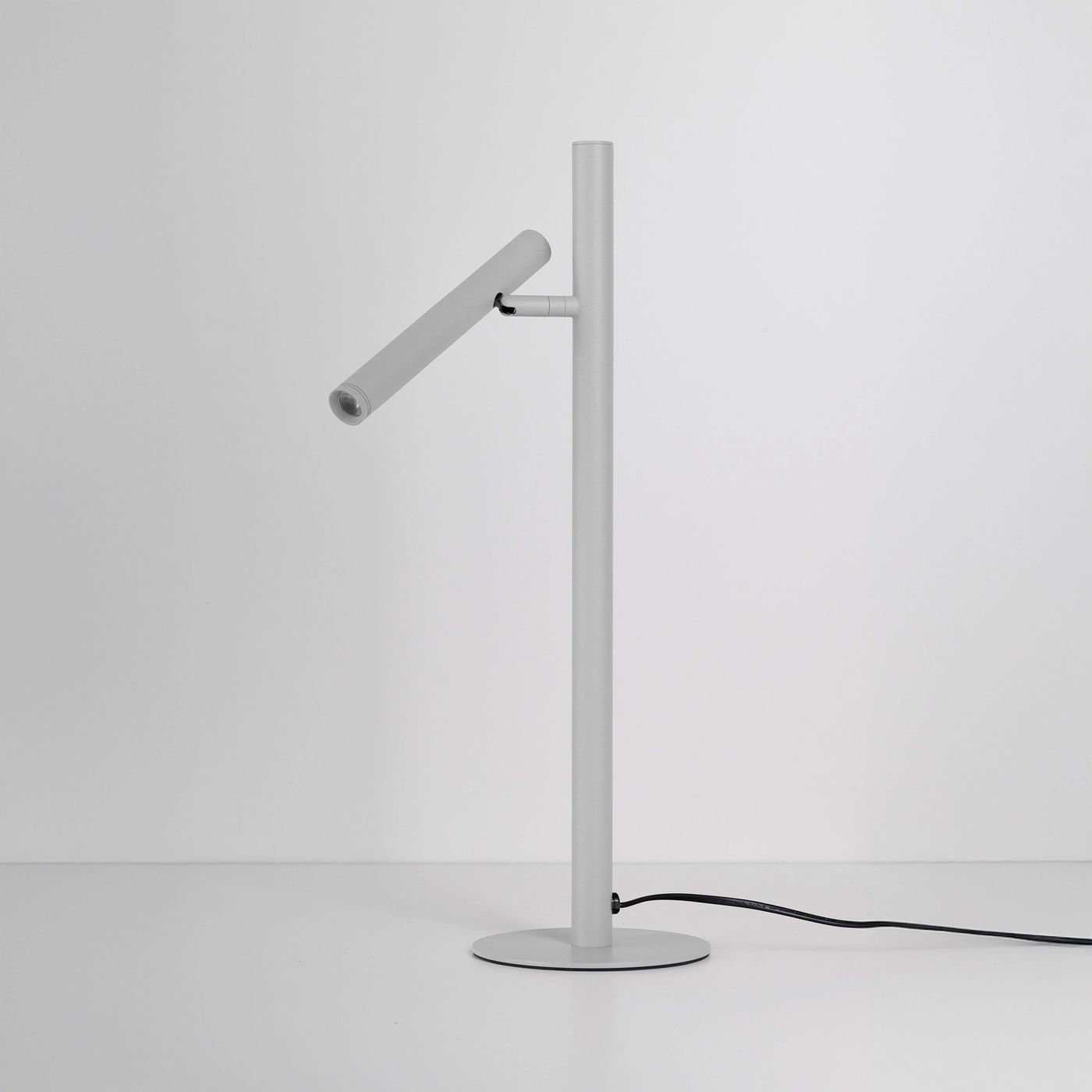 Lampa stołowa LED Trost 4,5W w kolorze białym, z prostą, metalową podstawą i regulowanym źródłem światła w formie cylindrycznego klosza. Ujęcie z boku, na gładkim, jasnym tle. Kabel zasilający widoczny przy podstawie.