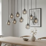 Lampa wisząca Cosmo 9-punktowa w kolorze grafitowym, z przezroczystymi kulistymi kloszami. Ujęcie pokazuje lampę zawieszoną nad drewnianym stołem, we wnętrzu. Klosze mają widoczne żarówki, a w tle zdjęcia znajduje się dekoracja kwiatowa w wazonie.
