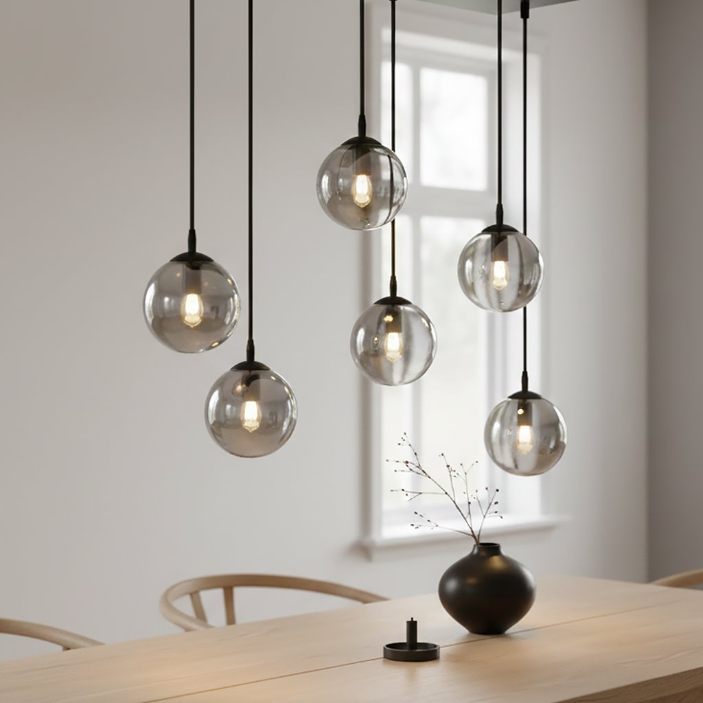 Lampa wisząca Cosmo 6-punktowa w kolorze grafitowym z sześcioma przezroczystymi kulami, zawieszona na długich czarnych kablach. Produkt umieszczony nad drewnianym stołem, w jasnym wnętrzu z oknami w tle.