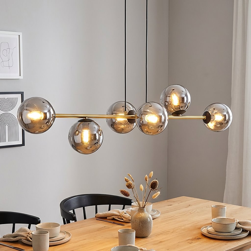 Lampa wisząca Gravity 6-punktowa w kolorze czarnym, złotym i grafitowym. Składa się z sześciu szklanych kul w różnych odcieniach, zawieszonych na złotej rurze, w aranżacji nad drewnianym stołem w jadalni.