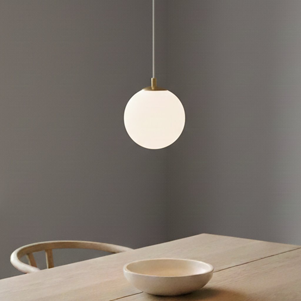 Lampa wisząca Royal 1-punktowa w białym szkle z złotym mocowaniem. Okrągły klosz zwisający z cienkiego kabla, umieszczony nad drewnianym stołem z ceramiczną misą. Tło w odcieniach szarości.