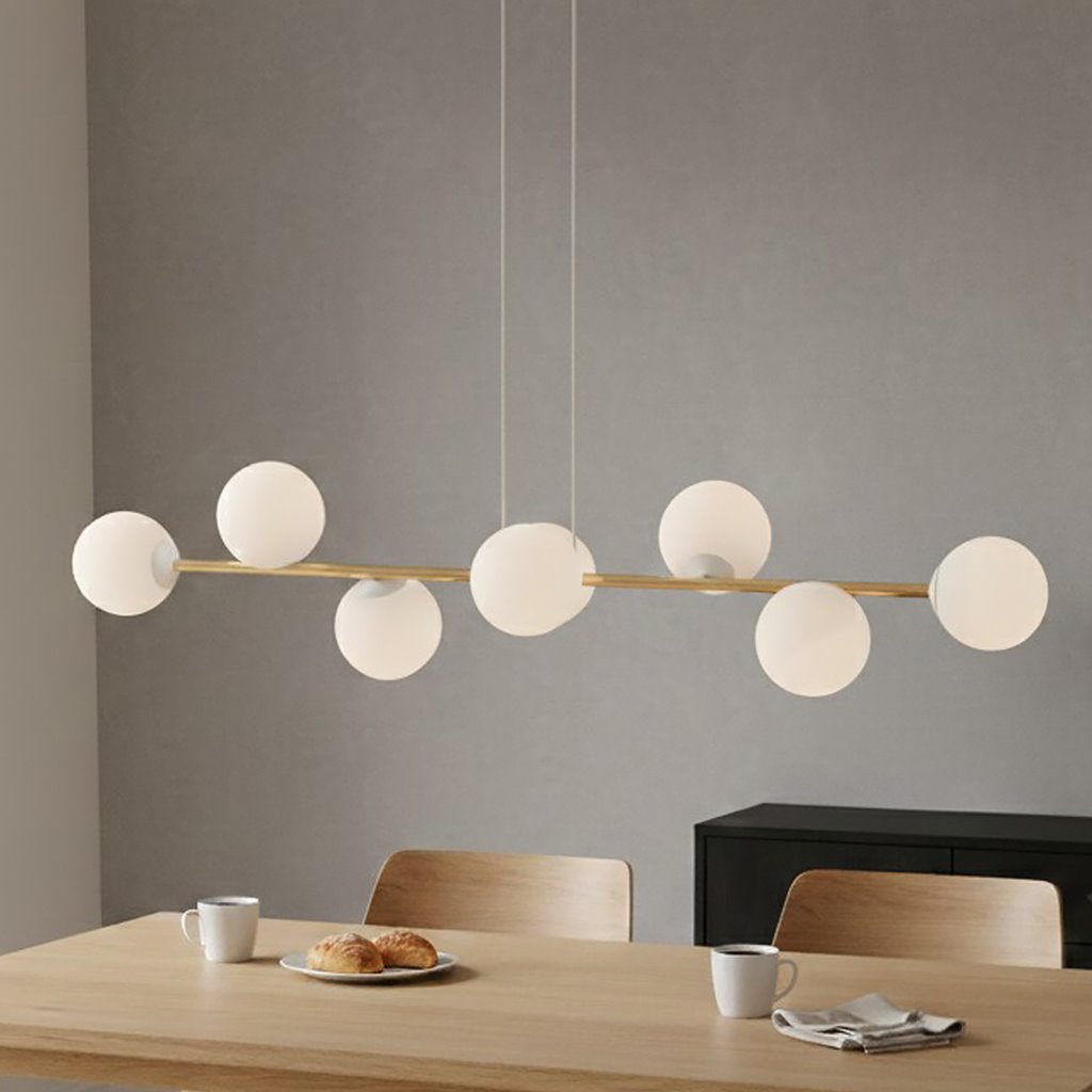Lampa wisząca Gravity 8-punktowa w białym i złotym wykończeniu, z opalowymi kloszami, zawieszona nad drewnianym stołem. Widoczna jest prosta konstrukcja z sześcioma okrągłymi kloszami na metalowej rurze, w minimalistycznym wnętrzu.