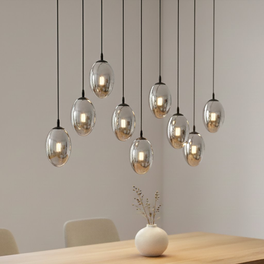 Czarna lampa wisząca Astral z dziewięcioma punktami świetlnymi, o owalnych, metalicznych kloszach. Wisząca na cienkich, czarnych kablach, zamontowana nad drewnianym stołem, w tle jasna ściana. Idealna do nowoczesnych wnętrz.