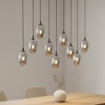 Czarna lampa wisząca Astral z dziewięcioma punktami świetlnymi, o owalnych, metalicznych kloszach. Wisząca na cienkich, czarnych kablach, zamontowana nad drewnianym stołem, w tle jasna ściana. Idealna do nowoczesnych wnętrz.
