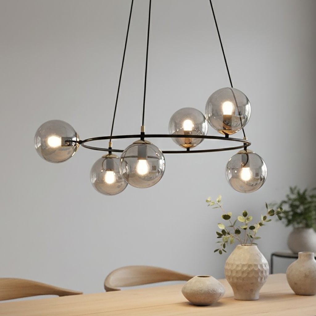 Lampa wisząca Azura z sześcioma oprawami E14, w kolorze czarnym i grafitowym. Okrągła konstrukcja z przezroczystymi kulami, zawieszona na długich linkach. Widoczna w nowoczesnym wnętrzu, na tle drewnianego stołu i ceramicznych wazonów.