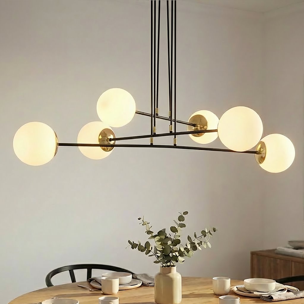 Lampa wisząca Ognis 6-punktowa w kolorze czarnym, z sześcioma okrągłymi, mlecznymi kloszami. Ujęcie z dołu, zawieszona nad stołem. W tle widoczne naczynia i dekoracja z gałązką eukaliptusa w wazonie.