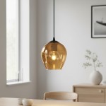 Lampa wisząca Istar 1-punktowa w miodowym kolorze z przezroczystym kloszem, zawieszona na czarnym kablu. Klosz ma zaokrąglony kształt i umieszczoną wewnątrz żarówkę, tworzącą przytulne oświetlenie. W tle widoczny stół i dekoracyjne elementy.