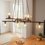 Lampa wisząca Essa 8-punktowa w kolorze czarnym i przezroczystym, z ośmioma kulistymi kloszami, umieszczona na stalowej konstrukcji. Wisi nad drewnianym stołem, w tle widoczne okno i jasne wnętrze.