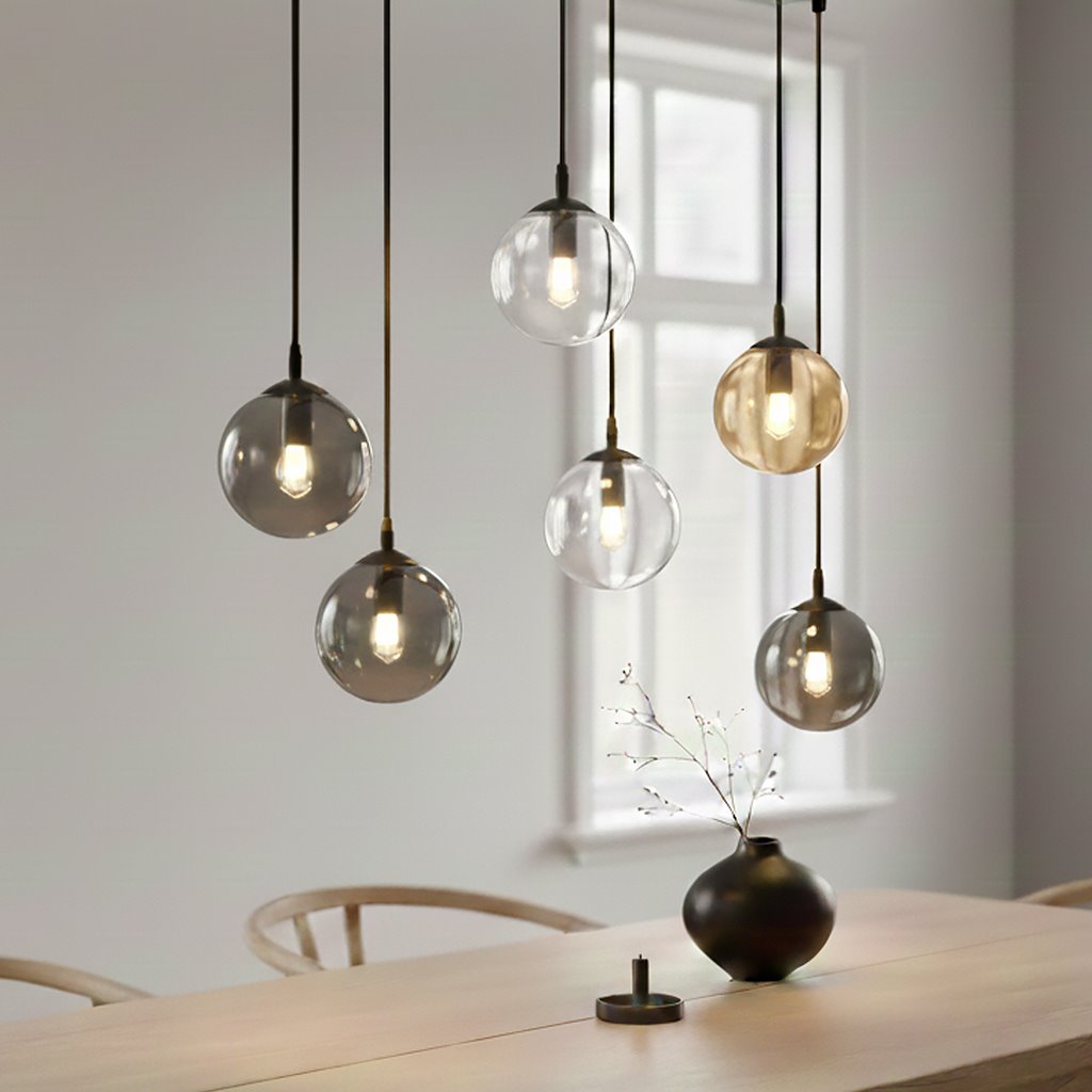 Lampa wisząca Cosmo mix, 6-punktowa, z przezroczystymi i matowymi kulami w odcieniach szarości i złota. Zawieszona na cienkich linkach, idealna do nowoczesnych wnętrz. Widoczna w aranżacji nad drewnianym stołem.