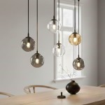 Lampa wisząca Cosmo mix, 6-punktowa, z przezroczystymi i matowymi kulami w odcieniach szarości i złota. Zawieszona na cienkich linkach, idealna do nowoczesnych wnętrz. Widoczna w aranżacji nad drewnianym stołem.