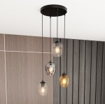 Lampa wisząca Istar Premium mix, 4-punktowa, z czarnym stelażem i czterema szklanymi kloszami w odcieniach przezroczystym, szarym i brązowym. Ujęcie z góry, zawieszona na długich przewodach, w tle drewniana ściana.