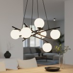 Lampa wisząca Essa 5-punktowa w kolorze czarnym z opalowymi kulami. Posiada pięć okrągłych kloszy zawieszonych na krzyżujących się metalowych prętach. Ujęcie z góry, w tle nowoczesne wnętrze z sofą i roślinnością.