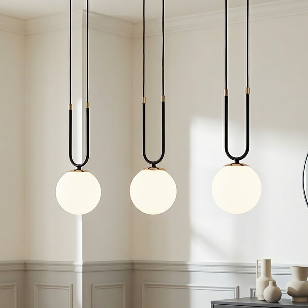 Czarna i biała lampa wisząca 3-punktowa Glam 1112/3 z okrągłymi, białymi kloszami zawieszonymi na długich, czarnych przewodach. Lampa umieszczona w jasnym wnętrzu, z widocznymi dekoracyjnymi elementami w tle.