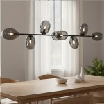 Lampa wisząca Pandora 8-punktowa w kolorze czarnym i grafitowym, z ośmioma szklanymi kloszami w kształcie owalnym, zawieszona na cienkiej metalowej konstrukcji, umieszczona nad drewnianym stołem w jasnym wnętrzu.