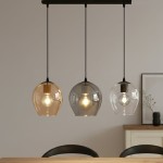 Lampa wisząca Istar mix 3-punktowa z trzema szklanymi kloszami w kolorach brązowym, szarym i przezroczystym, zawieszona na czarnych linkach. Klosze mają zaokrąglony kształt, a w środku widoczne żarówki, umieszczona nad drewnianym stołem w jasnym wnętrzu.