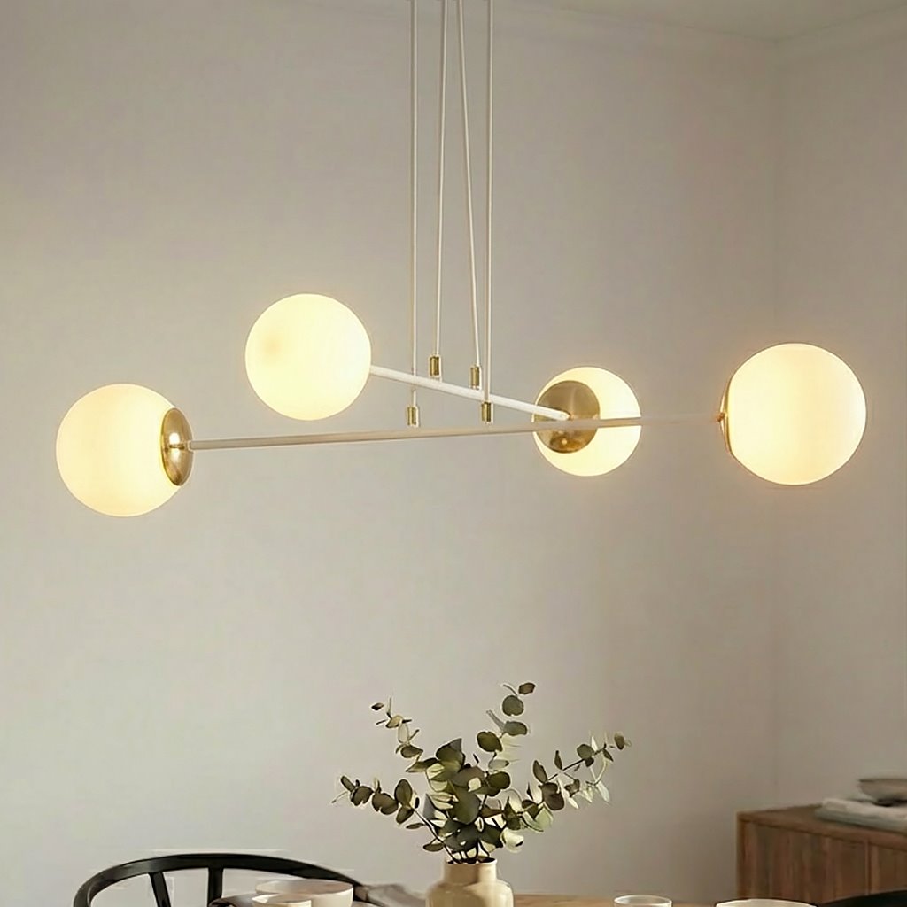 Lampa wisząca Ognis 4-punktowa w białym kolorze z okrągłymi kloszami w odcieniu ciepłej bieli. Klosze zawieszone na cienkich białych linkach, z metalowymi elementami w kolorze złotym. Lampa umieszczona w jasnym wnętrzu z roślinnością w tle.