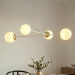 Lampa wisząca Ognis 4-punktowa w białym kolorze z okrągłymi kloszami w odcieniu ciepłej bieli. Klosze zawieszone na cienkich białych linkach, z metalowymi elementami w kolorze złotym. Lampa umieszczona w jasnym wnętrzu z roślinnością w tle.