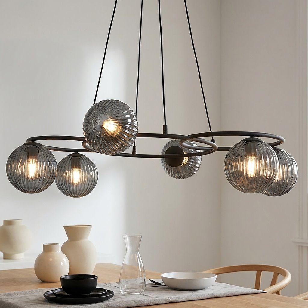 Lampa wisząca Libra z sześcioma kloszami E14 w kolorze czarnym i grafitowym. Klosze mają teksturowaną, szklaną powierzchnię, zawieszone na okrągłej konstrukcji z metalowymi elementami. Produkt umieszczony nad drewnianym stołem, w jasnym wnętrzu.