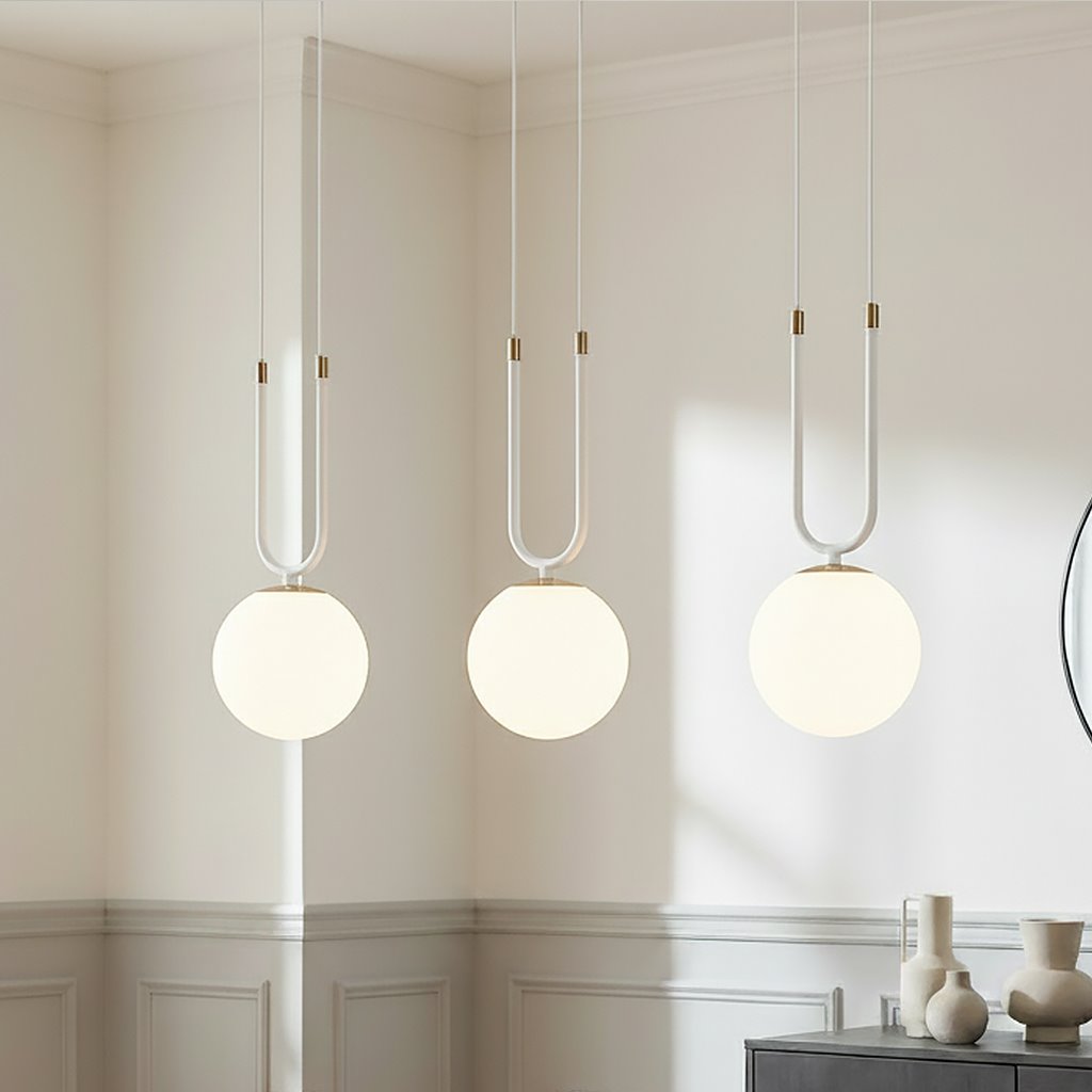 Lampa wisząca Glam 3-punktowa w białym kolorze z okrągłymi kloszami. Zawieszona na białych przewodach z dekoracyjnymi złotymi detalami. Widok frontalny, umieszczona w jasnym wnętrzu z minimalistycznym wystrojem.