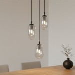 Lampa wisząca Astral 3-punktowa w kolorze czarnym i transparentnym, z trzema szklanymi kulami w kształcie owalu, zawieszona na cienkich kablach. Widoczna żarówka wewnątrz każdej kuli. Tło jasne, minimalistyczne, z drewnianym stołem i wazonem.