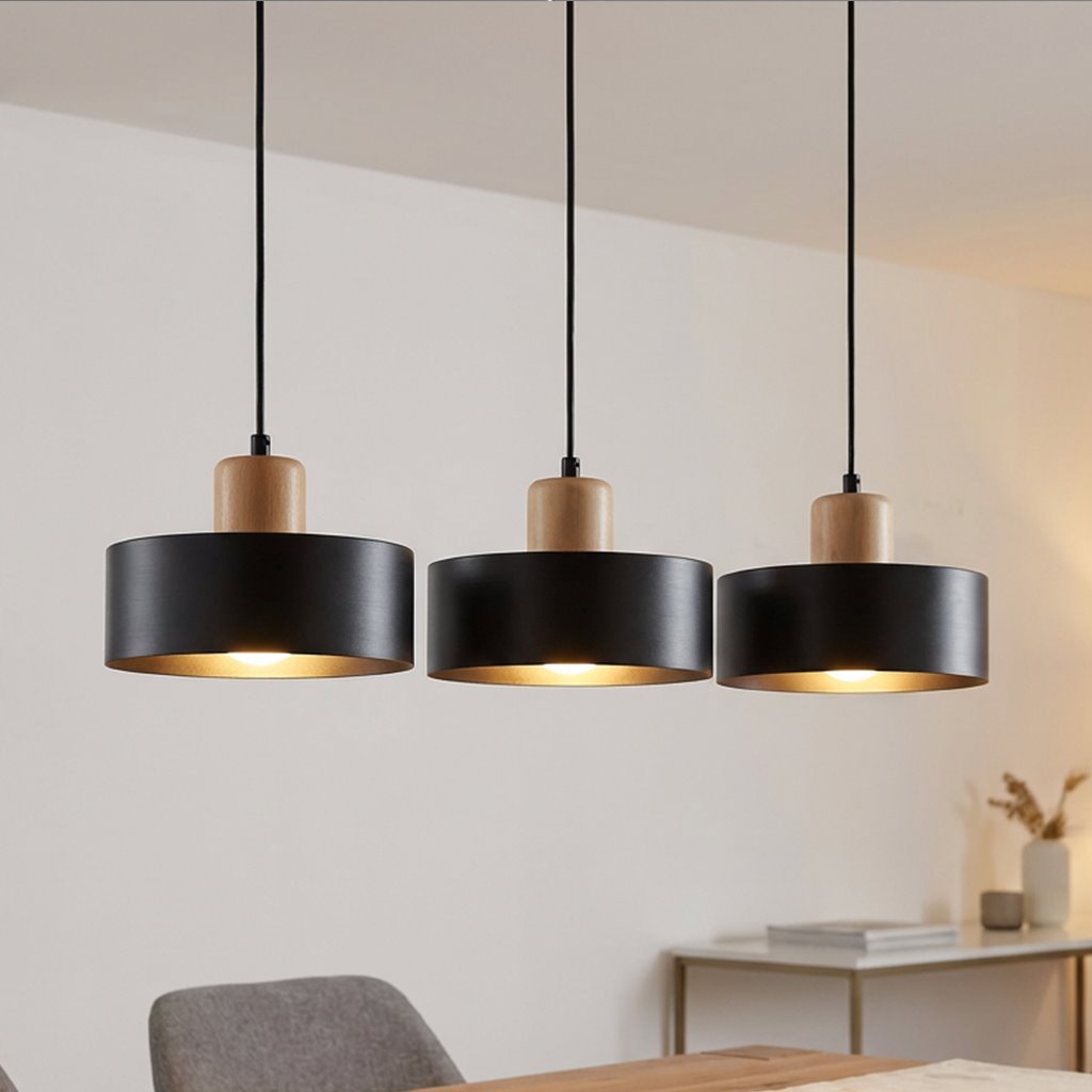 Lampa wisząca Torin 3-punktowa, czarna, z drewnianymi detalami. Posiada trzy okrągłe klosze na długich przewodach, w równym rozstawieniu. Klosze mają matowe wykończenie i złoty środek, co tworzy kontrast. Produkt umieszczony w jasnym wnętrzu.