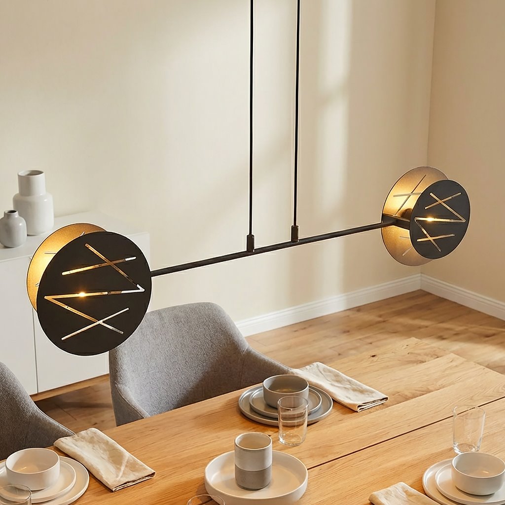 Lampa wisząca Xotic 2xE27 w kolorze czarnym, zawieszona na dwóch cienkich przewodach. Okrągłe klosze z dekoracyjnym wzorem w formie linii. Produkt umieszczony nad drewnianym stołem, w otoczeniu zastawy stołowej i dekoracji.