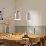 Lampa wisząca Bolero 2-punktowa w kolorze białym z drewnianymi detalami. Zawieszona nad drewnianym stołem, o nowoczesnym kształcie, w otoczeniu ceramicznych naczyń i dekoracji. Kąt ujęcia frontalny, ukazujący detale i kontekst użytkowania.