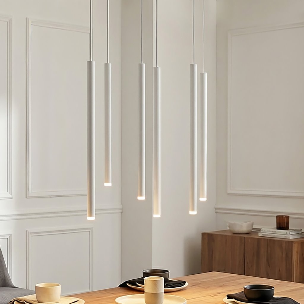 Lampa wisząca Selter 6-punktowa w białym kolorze, składająca się z sześciu smukłych, prostokątnych elementów świetlnych zawieszonych na cienkich linkach. Ujęcie frontalne, lampa wisi nad drewnianym stołem w jasnym wnętrzu.