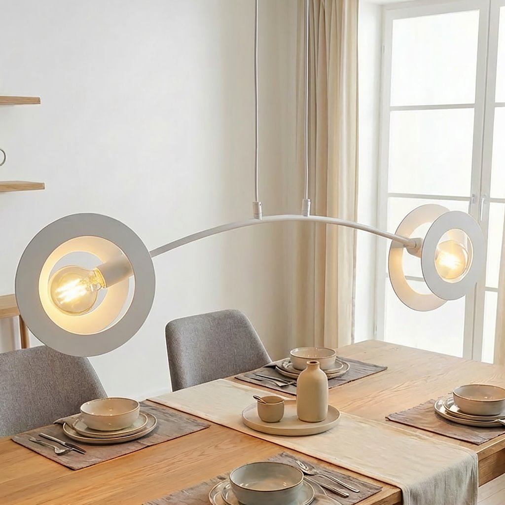 Lampa wisząca Euforia w kolorze białym z dwoma żarówkami E27, z subtelnymi okrągłymi kloszami, zawieszona nad drewnianym stołem w jadalni. Tło jasne, z zasłonami, w aranżacji z talerzami i naczyniami w neutralnych odcieniach.