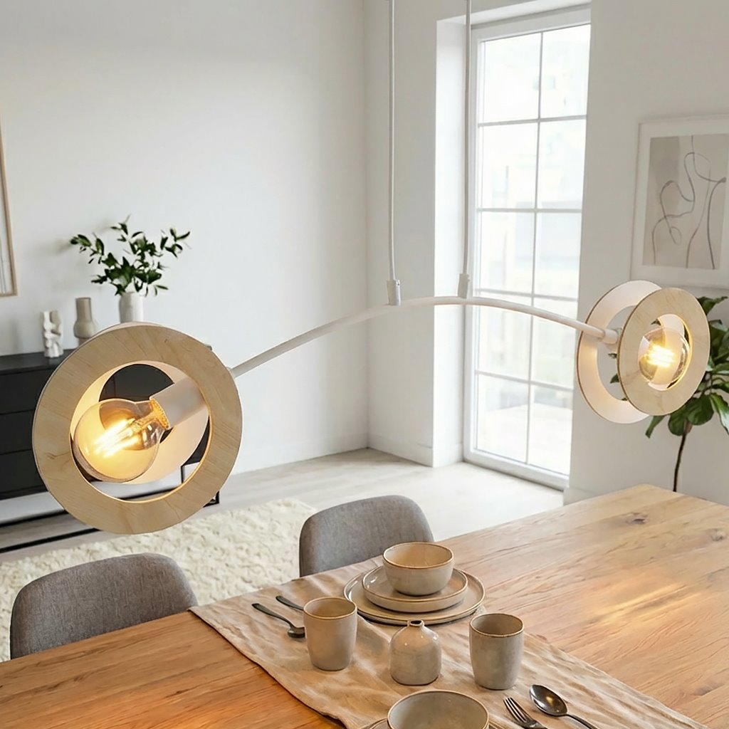 Lampa wisząca Skiva 2xE27 w kolorze białym i jasnego drewna, z dwoma okrągłymi kloszami, zawieszona na łukowatym stelażu. Widoczne wnętrze lampy z żarówkami oraz stół z filiżankami i talerzami w tle.
