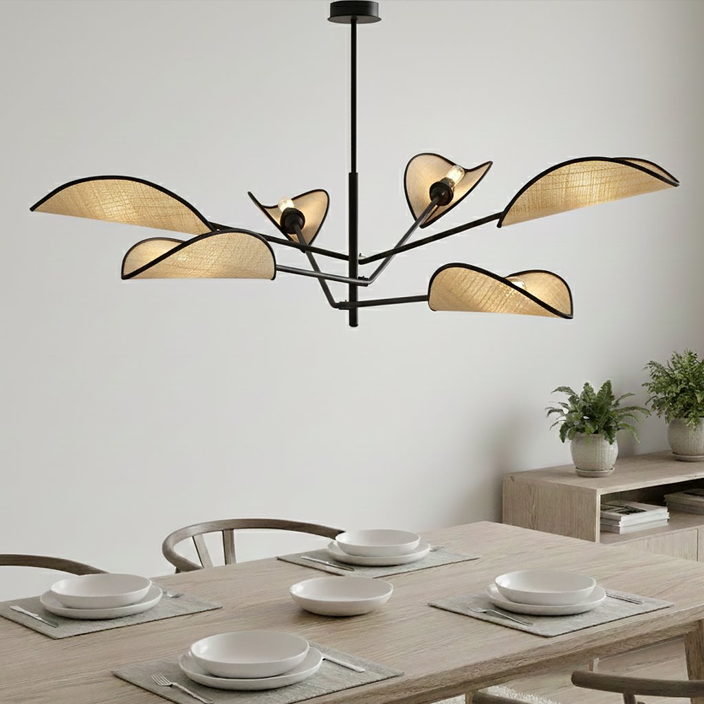 Lampa sufitowa Vene 6-punktowa w kolorze czarnym z elementami rattanowymi, złożona z sześciu kloszy w kształcie fal, wisząca nad drewnianym stołem, z talerzami i podkładkami. Tło jasne, minimalistyczne, z roślinnością obok.