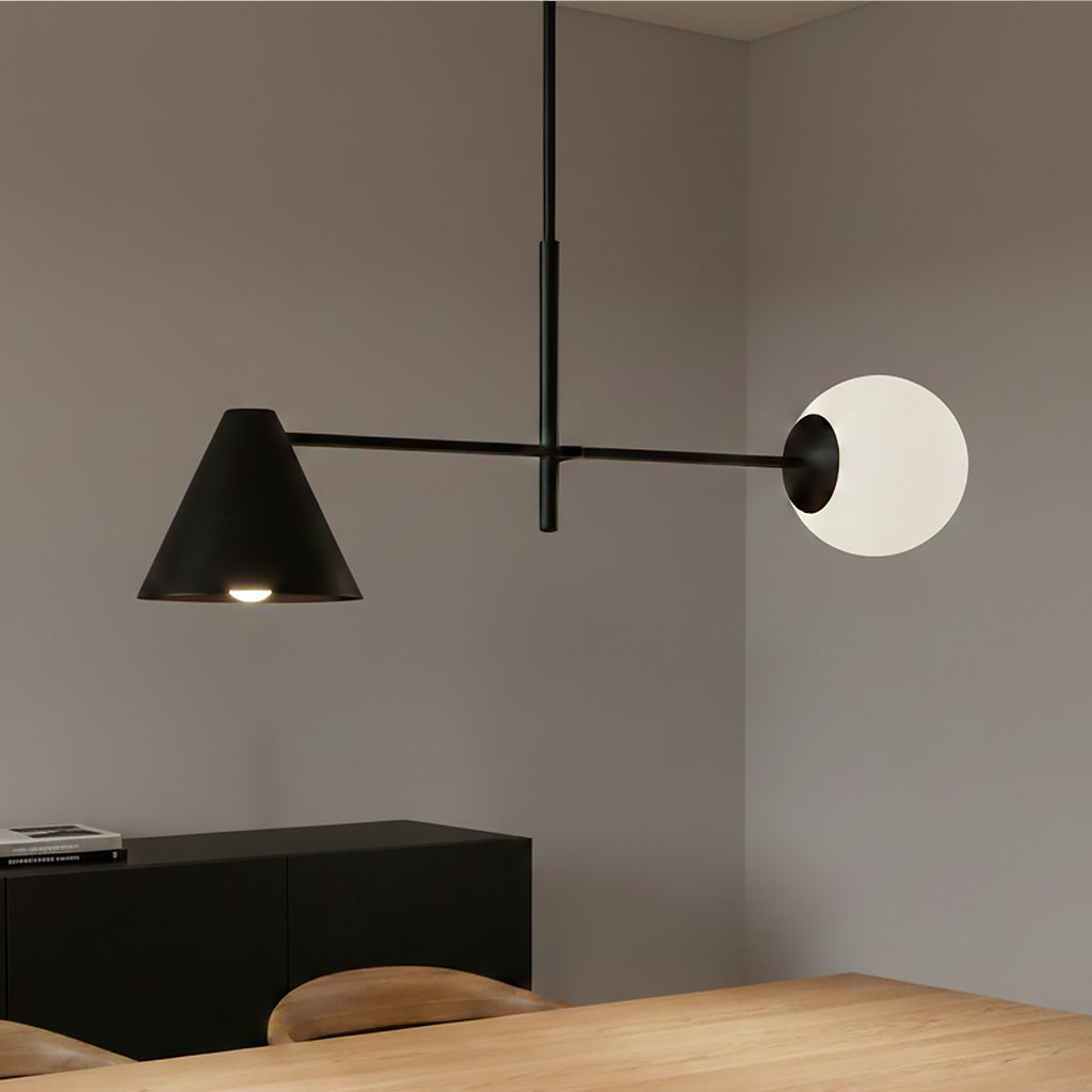 Lampa wisząca Hermes w kolorze czarnym z dwiema oprawami: stożkowa lampa E27 z białym kloszem oraz okrągła oprawa E14. Ujęcie z boku, zawieszona nad drewnianym stołem, z minimalistycznym tłem w odcieniach szarości.