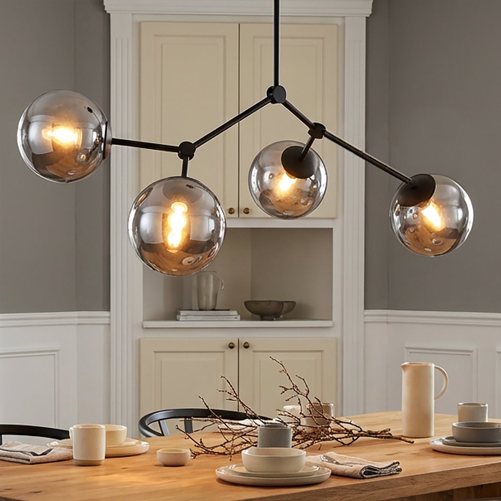 Czarna lampa sufitowa 4-punktowa z grafitowymi, przezroczystymi kloszami, zawieszona nad drewnianym stołem. Klosze mają okrągły kształt, w środku żarówki emitujące ciepłe światło. Tło w jasnym kolorze, z zabudową kuchenną.