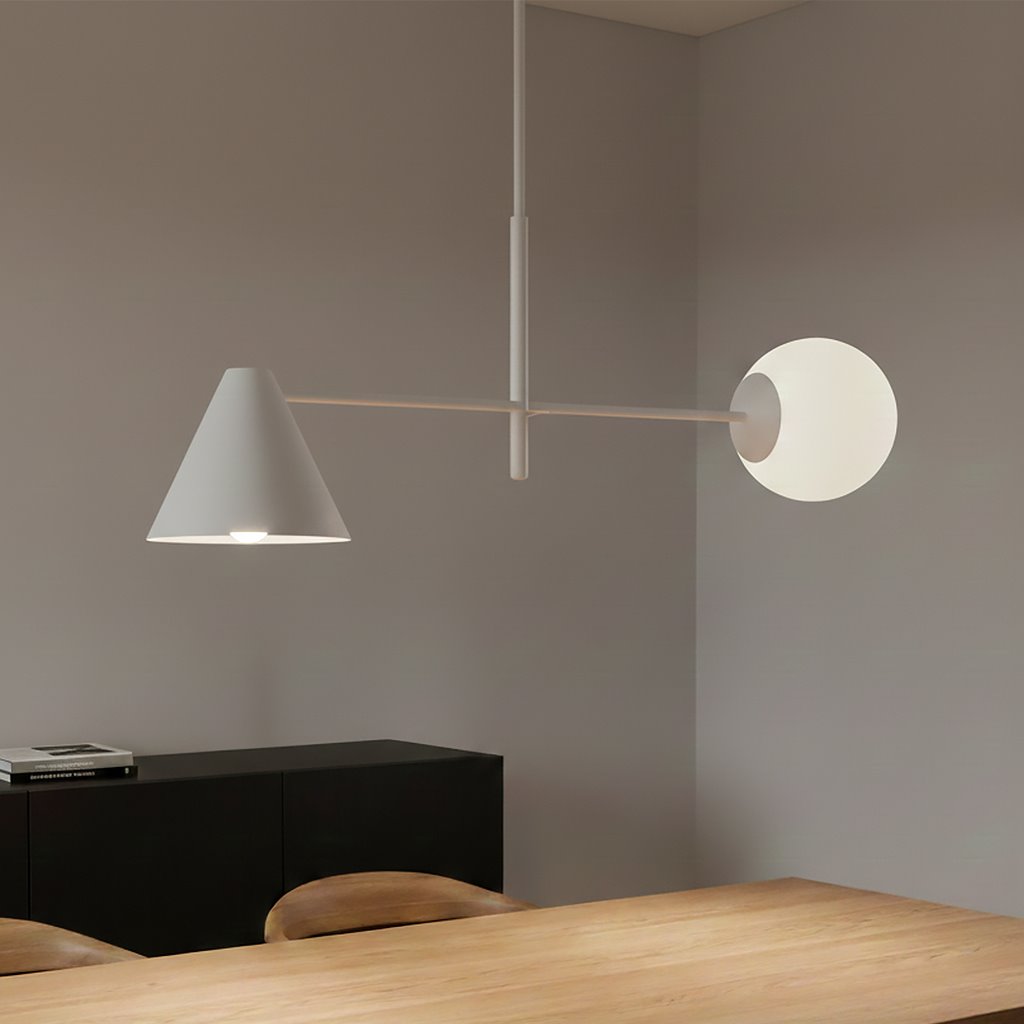 Lampa wisząca Hermes w kolorze białym z dwoma kloszami: stożkowym i okrągłym. Klosze zawieszone na cienkim, metalowym ramieniu. Produkt zamontowany nad drewnianym stołem w minimalistycznym wnętrzu.
