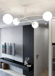 Biała lampa sufitowa 4-punktowa Pregos z okrągłymi kloszami, zamontowana na suficie. Klosze rozmieszczone na cienkich ramionach, tworzą nowoczesny design. Tło z szarymi ścianami i telewizorem w aranżacji wnętrza.