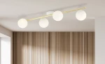 Lampa sufitowa 4-punktowa w kolorze białym i złotym z opalowymi kloszami. Ułożona równolegle, z czterema okrągłymi kloszami, mocowana do sufitu. Tło w jasnym kolorze z drewnianą, pionową fakturą.