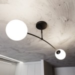 Czarna lampa sufitowa Pregos 2-punktowa z dwoma okrągłymi kloszami w białym kolorze, zamontowana na suficie. Klosze są zawieszone na cienkim, zakrzywionym ramieniu, co nadaje nowoczesny wygląd. Widoczna faktura sufitu betonowego.
