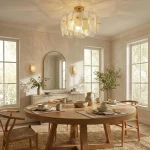 Lampa wisząca Richmond 6xE14 w kolorze mosiężnym, o kształcie okrągłym z przezroczystymi kloszami, zawieszona w jasnym wnętrzu nad okrągłym stołem. W tle widoczne okna, lustro oraz dekoracyjne dodatki.