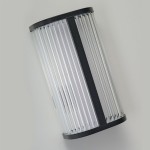 Kinkiet LED Pandora 11W CCT IP44 w kolorze czarnym, o cylindrycznym kształcie, wykonany z przezroczystego materiału, z poziomymi żłobieniami. Ujęcie pod kątem, wiszący na jednolitym tle. Idealny do użytku wewnętrznego i zewnętrznego.