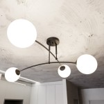 Czarna lampa sufitowa 4-punktowa Pregos z czterema okrągłymi, białymi kloszami. Ułożona w formie łuków, montowana do sufitu, z widocznym metalowym mocowaniem. Tło w odcieniach szarości z minimalistycznym wystrojem wnętrza.