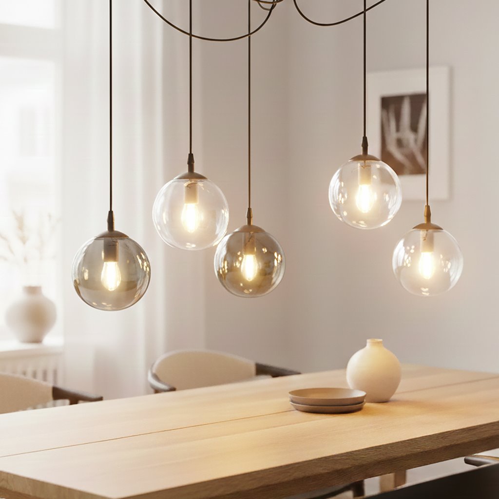 Lampa wisząca Gigi 5-punktowa w multikolorze z pięcioma szklanymi kulami na cienkich kabelkach. Kule mają różne odcienie, emitując ciepłe światło. Produkt wisi nad drewnianym stołem w jasnym wnętrzu.