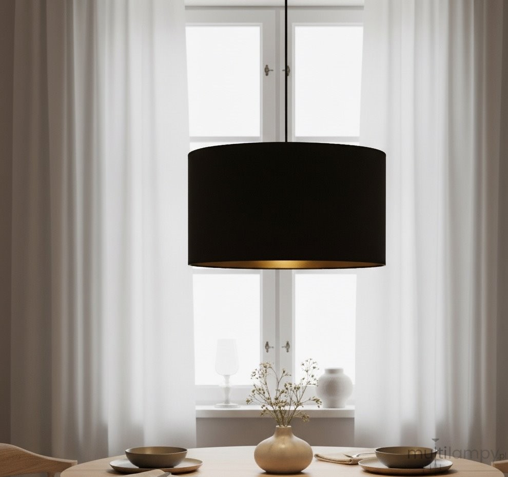 Czarna lampa wisząca Hilde 1-punktowa o cylindrycznym kształcie z matowym wykończeniem, zawieszona na cienkim przewodzie. Wnętrze klosza w kolorze złotym. Produkt umieszczony nad okrągłym drewnianym stołem, w otoczeniu zasłon i dekoracji.