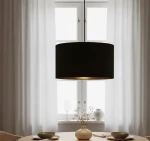 Czarna lampa wisząca Hilde 1-punktowa o cylindrycznym kształcie z matowym wykończeniem, zawieszona na cienkim przewodzie. Wnętrze klosza w kolorze złotym. Produkt umieszczony nad okrągłym drewnianym stołem, w otoczeniu zasłon i dekoracji.