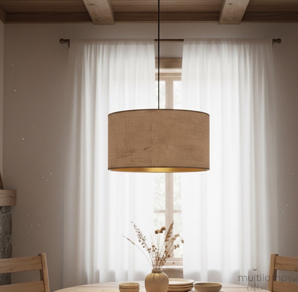 Różowa lampa wisząca Hilde 1-punktowa z okrągłym kloszem, zawieszona na cienkim przewodzie. Klosz wykonany z materiału o teksturze przypominającej len, z widoczną złotą wewnętrzną stroną. Lampa umieszczona nad drewnianym stołem w jasnym wnętrzu.