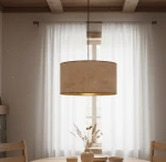 Różowa lampa wisząca Hilde 1-punktowa z okrągłym kloszem, zawieszona na cienkim przewodzie. Klosz wykonany z materiału o teksturze przypominającej len, z widoczną złotą wewnętrzną stroną. Lampa umieszczona nad drewnianym stołem w jasnym wnętrzu.