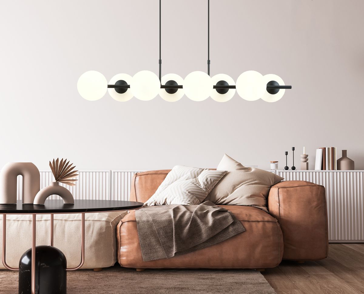 Lampa wisząca Rory 8-punktowa w kolorze czarnym z opalowymi kloszami. Zawieszona nad brązową sofą, z sześcioma okrągłymi kloszami na czarnych uchwytach. Otoczenie minimalistyczne, z okrągłym czarnym stołem i dekoracjami na białej komodzie.