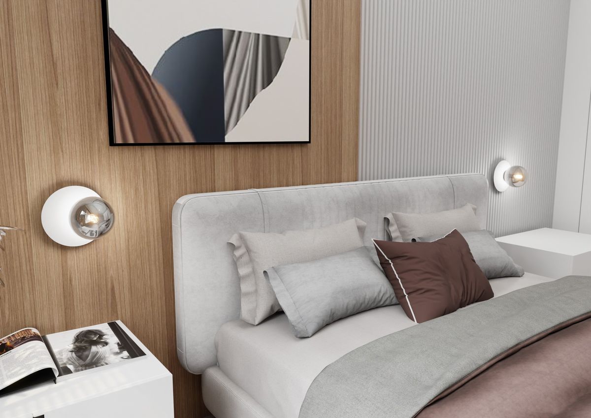 Oslo kinkiet 1-punktowy w kolorze białym z grafitowym akcentem, zamontowany na ścianie obok łóżka. Okrągła oprawa z metalowym wykończeniem, z widoczną żarówką w środku. W tle drewniana ściana i nowoczesne wnętrze sypialni z poduszkami i stolikiem nocnym.