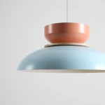 Lampa wisząca Aldo z jedną oprawą E27 w kolorze błękitnym i koralowym. Posiada okrągły klosz z matowej stali, z drewnianą podstawą. Zawieszona na białym przewodzie, ukazuje nowoczesny design w minimalistycznym stylu.